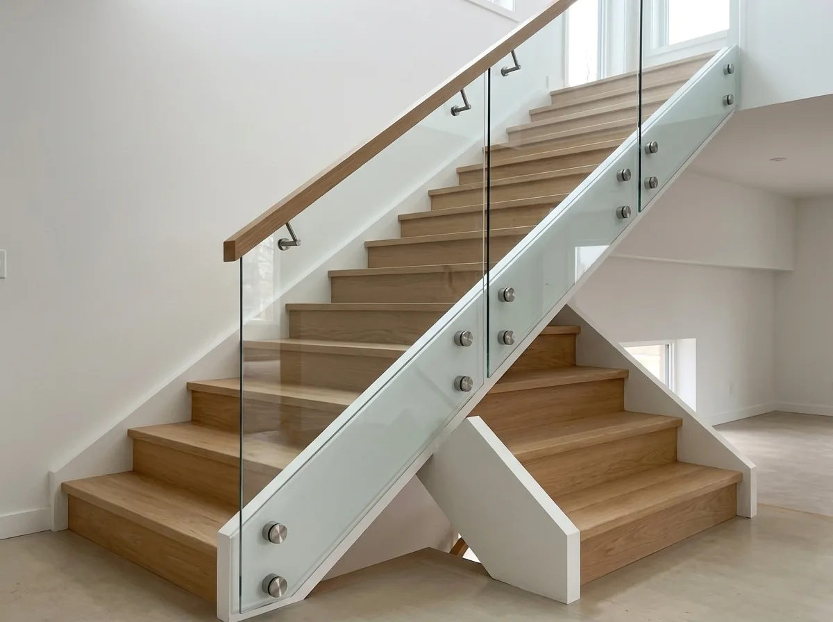 Clear glass panels fixed with round stainless standoff pins to the side of a wood stair stringer