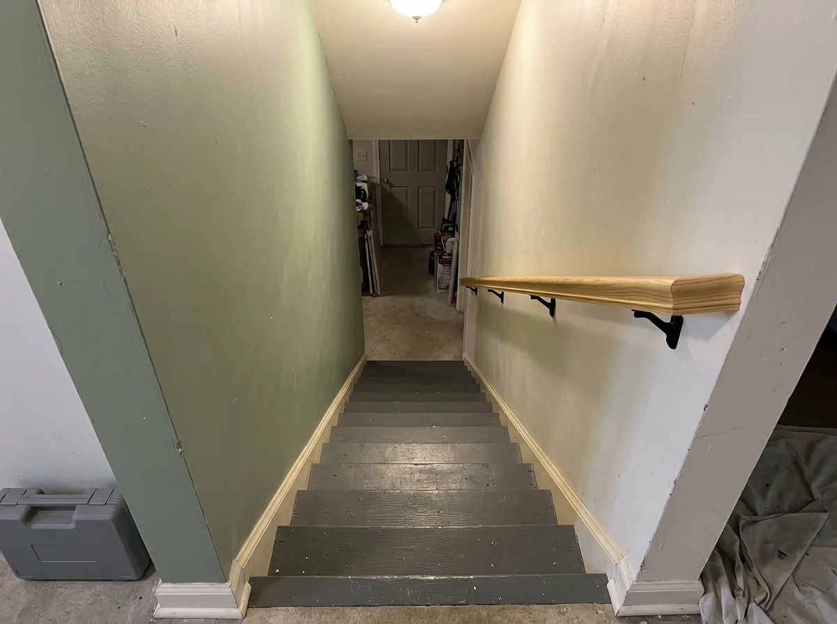 Pine handrail on black brackets beside a basement stair between two walls
